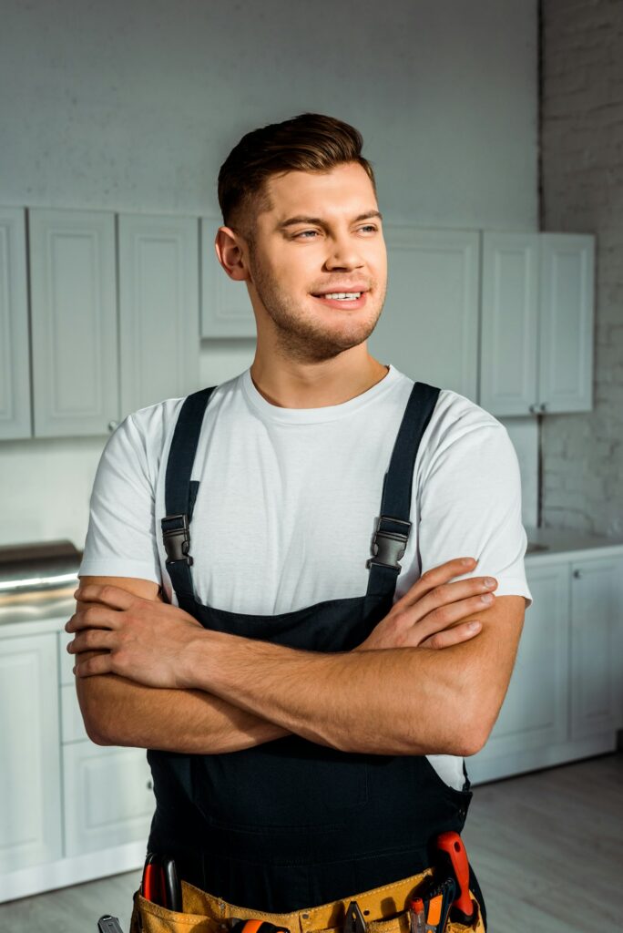 cheerful installer in overalls standing with crossed arms